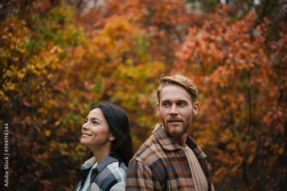 Beautiful happy couple smiling while standing back to back in forest Beautiful happy couple smiling while standing back to back in forest