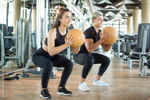 Young fitness couple in sportswear exercising with pilates ball at gym. Sporty man and woman workout together in health club.
