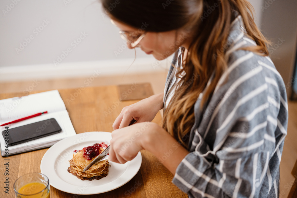 Smiling beautiful woman eating pancakes while having breakfast