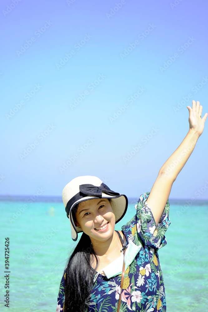 Asian women(half body) smiling happily raising their arms, wearing a floral blouse, woman hat with black ribbon,background is blue sky and a light green sea, holiday travel concept,with copy space.

