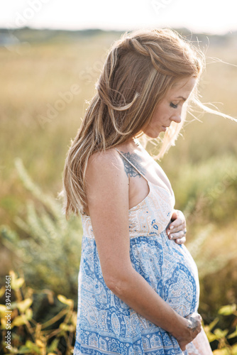 Profile view of the winsome red haired pregnant woman in long summer dress walking on the meadow.