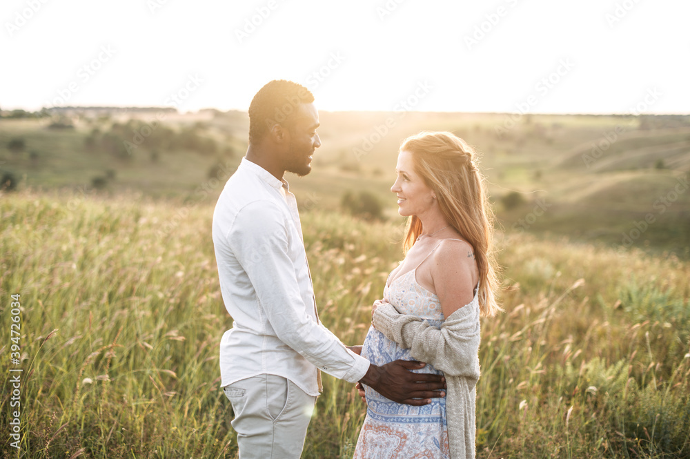 Sun rays shine through a pregnant couple. Tenderly future parents enjoying time together outdoors