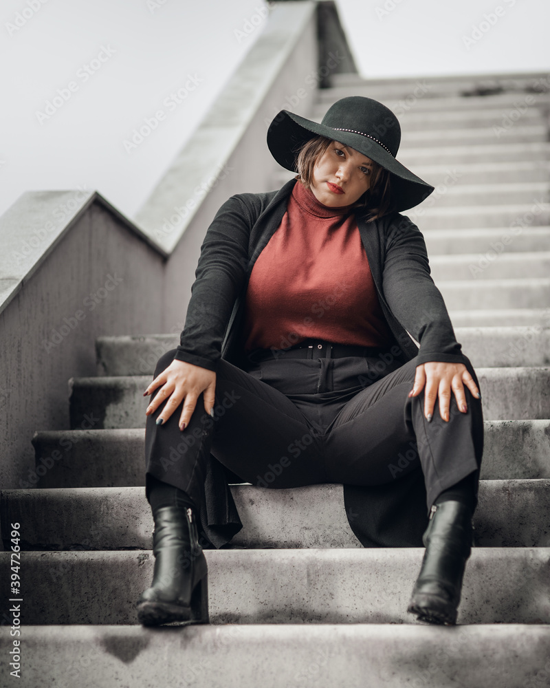 Brunette woman in hat sitting on the stairs of building in city