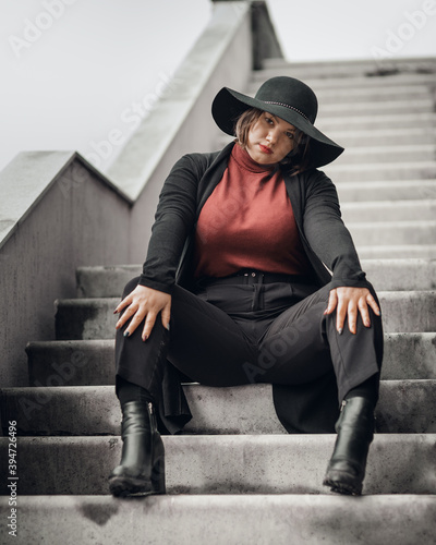 Obraz na płótnie Brunette woman in hat sitting on the stairs of building in city w salonie