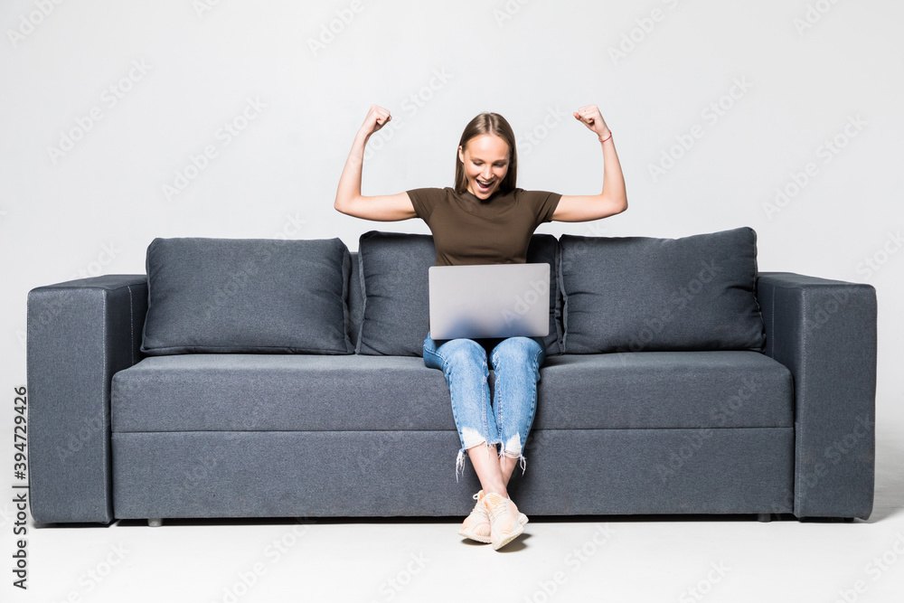 Happy young woman using laptop sitting at sofa with win gesture on white background Happy young woman using laptop sitting at sofa with win gesture on white background