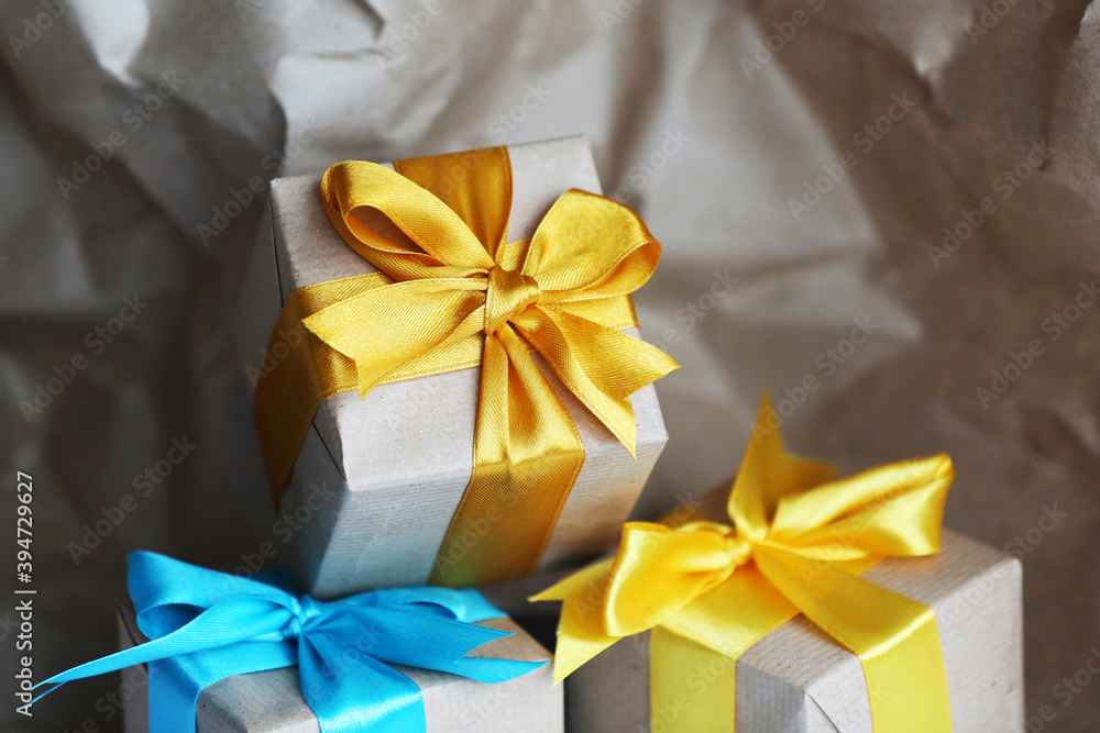 Three gift boxes wrapped by kraft brown paper with beautiful yellow and blue satin ribbons. Universal gifts design for all kind of celebration. Sustainable Christmas. Zero waste concept Three gift boxes wrapped by kraft brown paper with beautiful yellow and blue satin ribbons. Universal gifts design for all kind of celebration. Sustainable Christmas. Zero waste concept