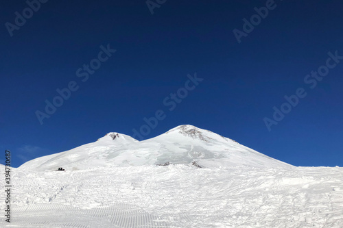 two peaks of Elbrus mountain in Caucasus in winter and background of deep blue sky. The highest european mountain attracts tourists.