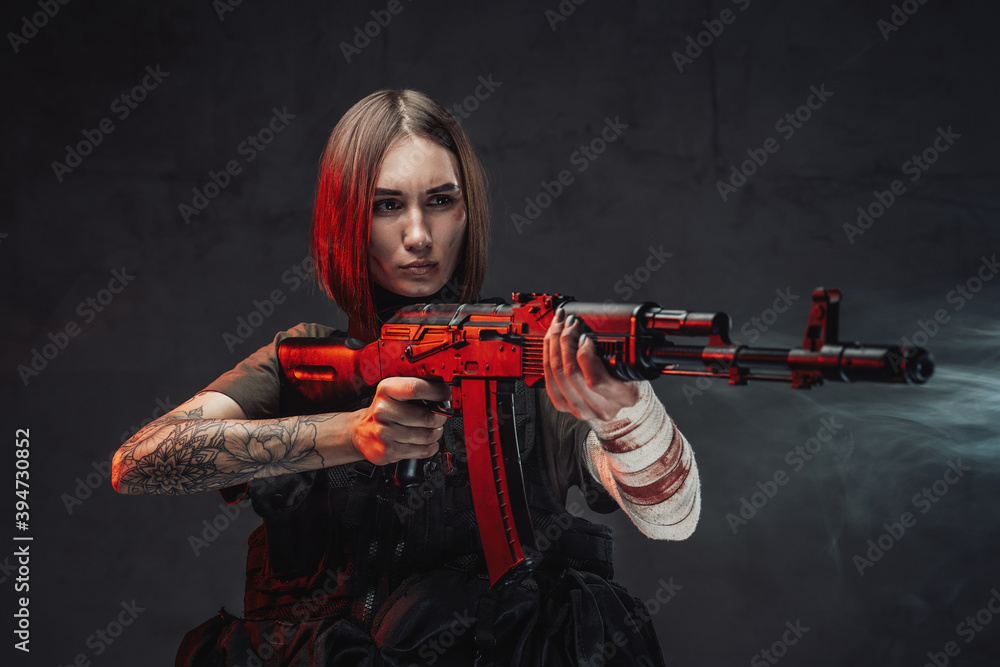 Dressed in black armour and dark shirt seductive martial woman with short haircut aims with rifle in dark background. Dressed in black armour and dark shirt seductive martial woman with short haircut aims with rifle in dark background.