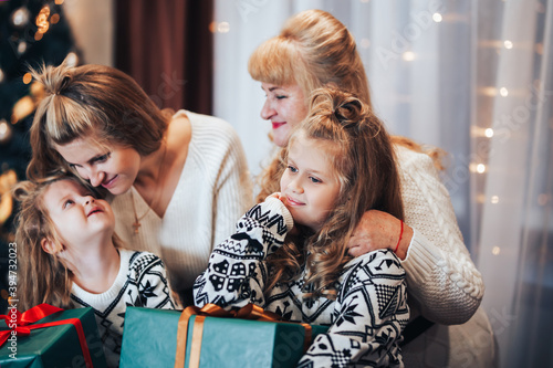 Children with mother and grandmother in their hands holding boxes with gifts in green packaging. Christmas mood. Celebrate the holiday with the whole family. Generation of women