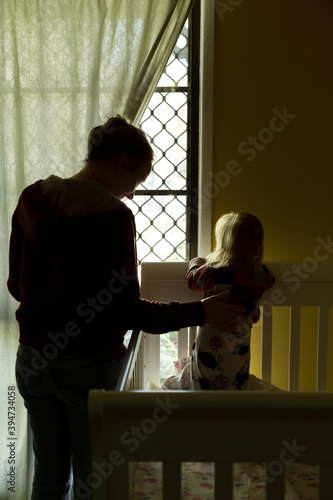 Mother and baby daughter in the bedroom as she stands and looks out window. photo