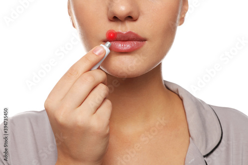 Woman with herpes applying cream onto lip against white background, closeup