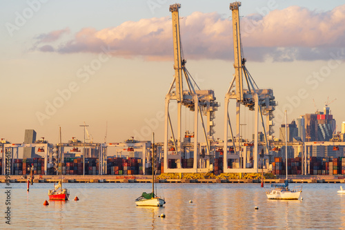 Small boats anchored in front of large gantry cranes at a city port at sunset. photo