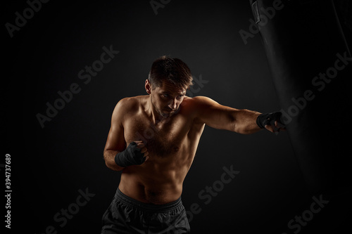 Male boxer punching in boxing bag on black background