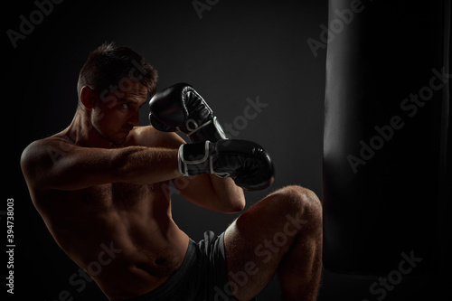 muscular boxer in black boxing gloves punching in boxing bag on dark background © producer