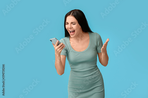 Stressed young woman with mobile phone on color background