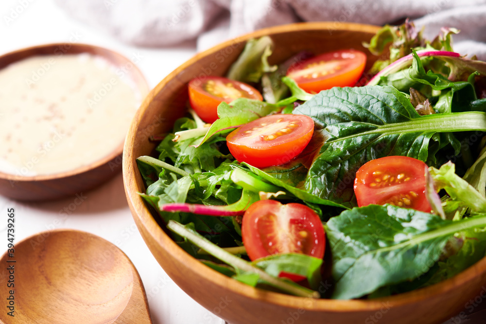 close up green salad from green leaves and cherry tomato in wooden bowl on white stone background close up green salad from green leaves and cherry tomato in wooden bowl on white stone background