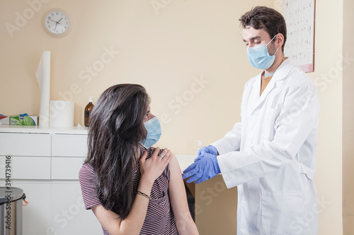 White woman with long hair wearing protective mask looking to the camera while being vaccinated by a doctor using gloves. Vaccine for the pandemics concept.