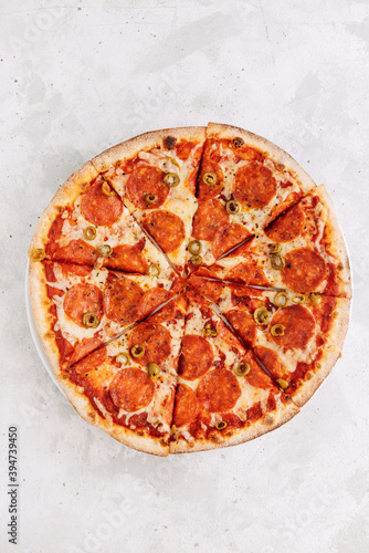 Pizza with pepperoni, cheese, tomatoes and olives on a light background, top view