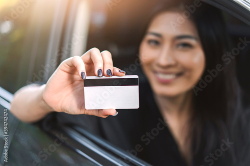 Asian woman buying or renting rental new car owner holding drivers license identification ID, taking and passing driving license examination test, happy cheerful smiling excited sold car dealership photo