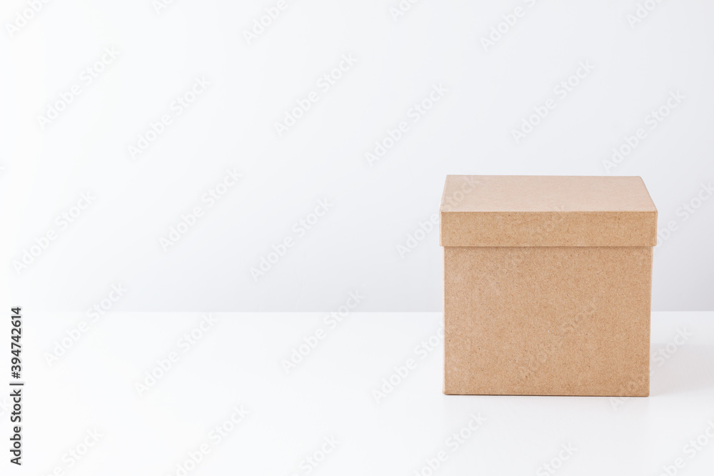 Closed cardboard box on a white table on the back of a white wall. Gift concept. Place for text. Closed cardboard box on a white table on the back of a white wall. Gift concept. Place for text.
