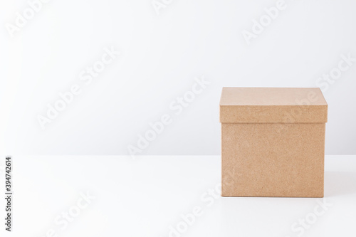 Closed cardboard box on a white table on the back of a white wall. Gift concept. Place for text.