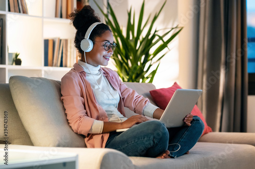 Schilderij op canvas Beautiful young entrepreneur woman working with laptop while listening music with headphones sitting on couch in the office