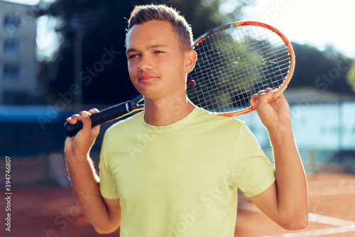 Young man teenager with tennis racket standing near net on clay court © fotofabrika