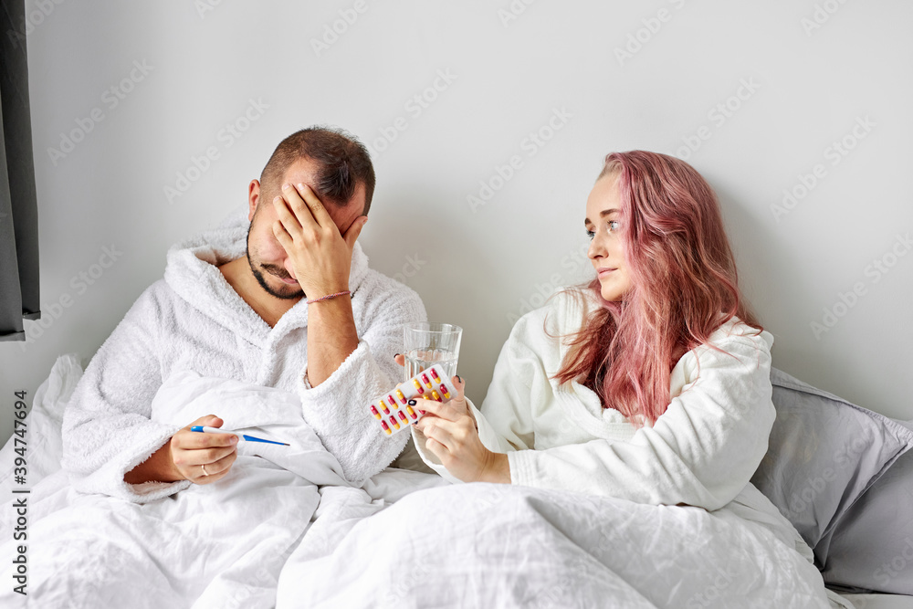 sick male has temperature and headache lying on bed, woman supports him, give medications sick male has temperature and headache lying on bed, woman supports him, give medications