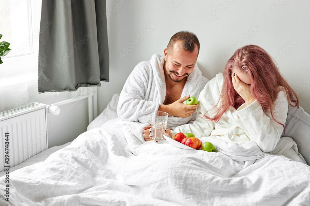 happy couple enjoy breakfast on bed, they laugh while eating fresh apples, joyful time in the morning, at home. love concept