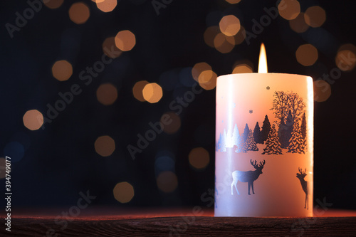 White Christmas candle on a wooden table with garlands background