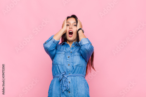 young woman looking unpleasantly shocked, scared or worried, mouth wide open and covering both ears with hands photo