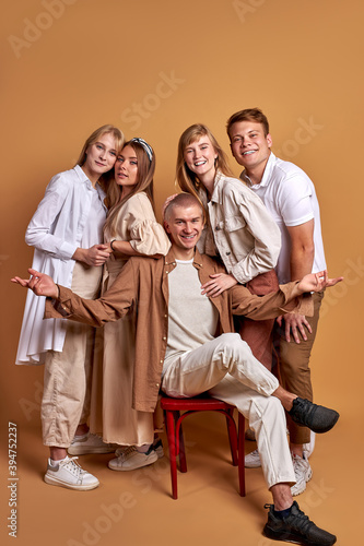 portrait of trendy stylish youth posing at camera isolated on brown background, handsome male and beautiful females in fashionable brown clothes stand together, models