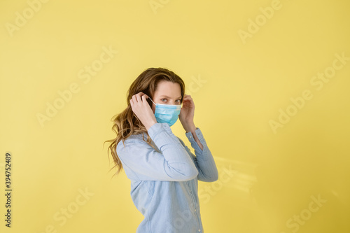 Beautiful caucasian brunette woman in protective medical mask on her face isolated standing on yellow background 