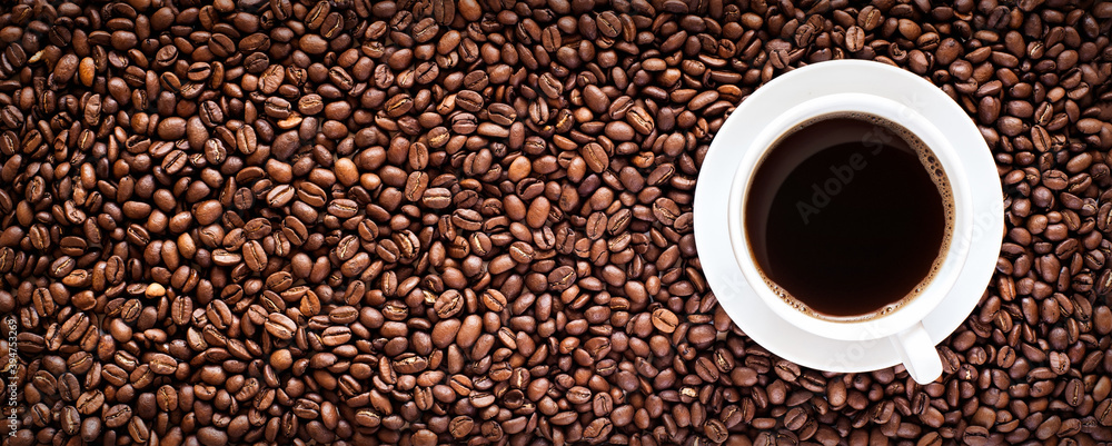 Roasted coffee bean background with a cup of hot espresso in the right side. Horizontal panorama banner with copy space
