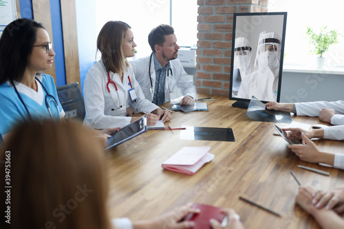 Doctors at meeting communicating via video communication with colleagues in protective overalls. Remote assistance telemedicine concept photo