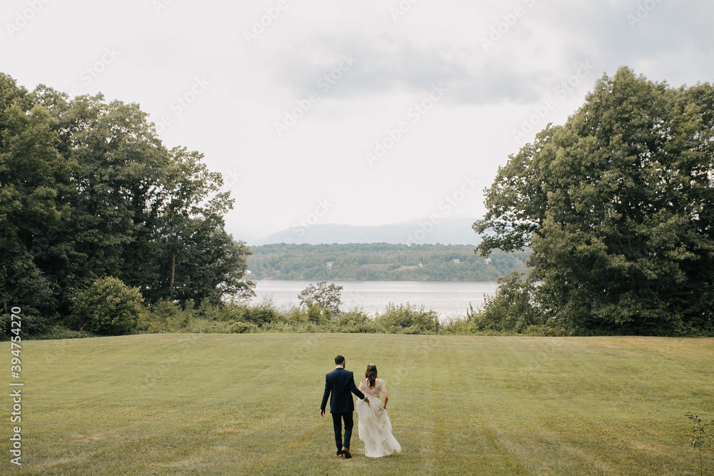 bride and groom walk toward water in the middle of a meadow on cloudy day bride and groom walk toward water in the middle of a meadow on cloudy day