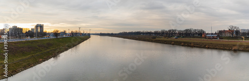 Cloudy panorama of Odra river between green coasts of city at sunset © wierzchu92