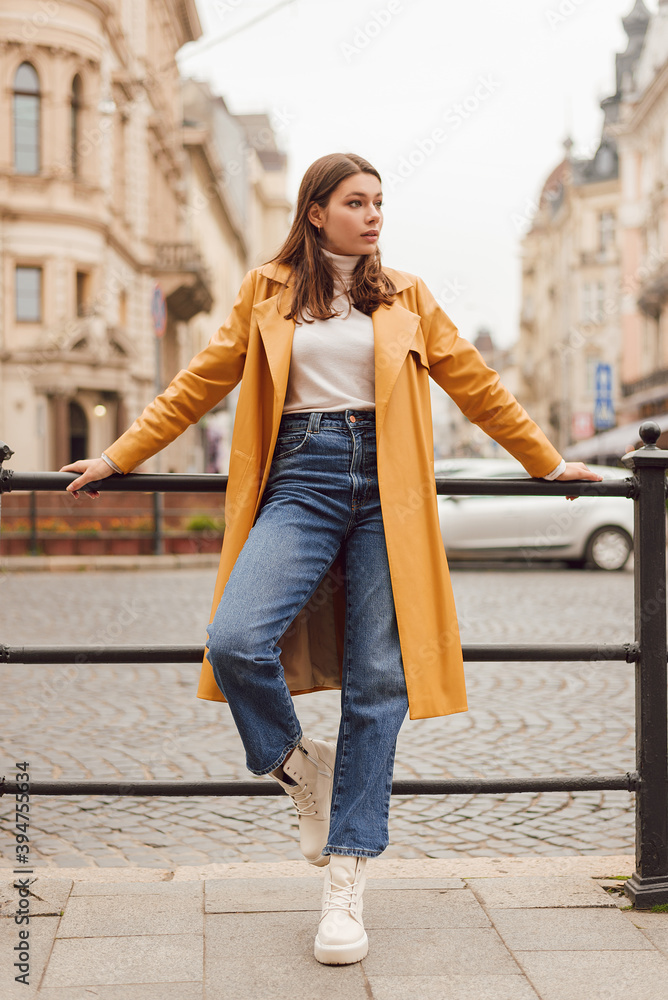 Young woman wearing stylish trendy yellow leather trench coat. Casual outfit