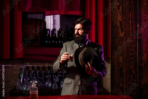 Serious man with glass of brandy. Vintage worker man with long beard holding whiskey. Sitting in bar.