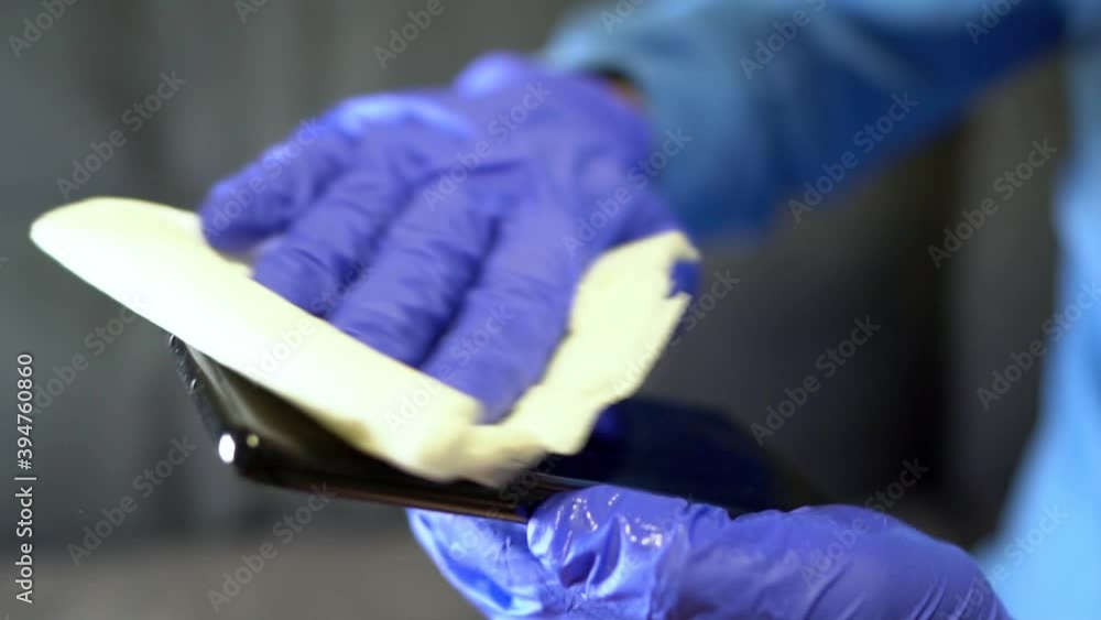 Hand in protective glove with napkin cleaning mobile phone. Covid-19 disinfection concept. Hand in protective glove with napkin cleaning mobile phone. Covid-19 disinfection concept.