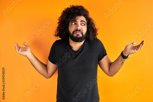 doubtful arab male is misunderstanding, show his incomprehension expression at camera, isolated over orange background photo