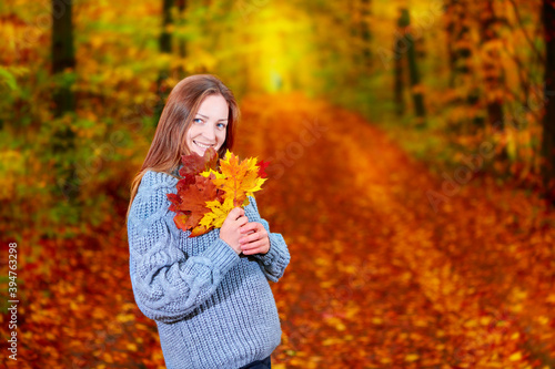 Girl with leaves in her hands in the autumn forest posing for the camera.