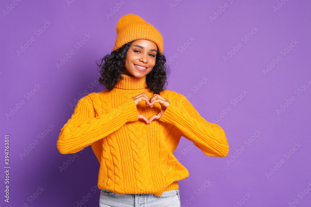 cheerful ethnic woman in yellow sweater and hat shape hearts to camera and express love and gratitude, confess in good feelings on colorful purple background cheerful ethnic woman in yellow sweater and hat shape hearts to camera and express love and gratitude, confess in good feelings on colorful purple background