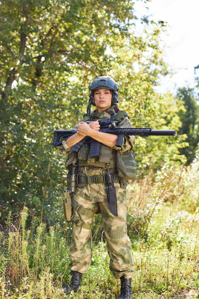 powerful sportive woman soldier ready for battle wearing protective military gear weapon, rifle or gun. in wild nature
