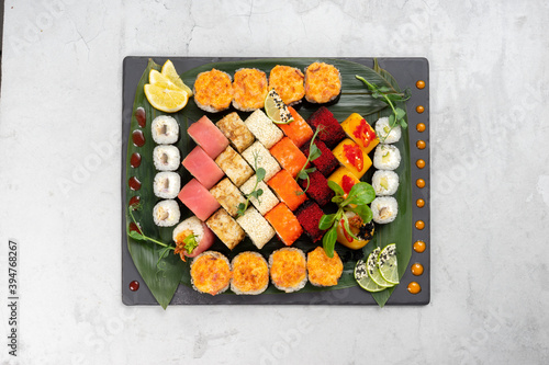 Big beautiful set of different types of sushi maki on a black rectangular stone slate plate. A traditional Japanese dish of raw fish and seafood wrapped in boiled rice and nori seaweed.