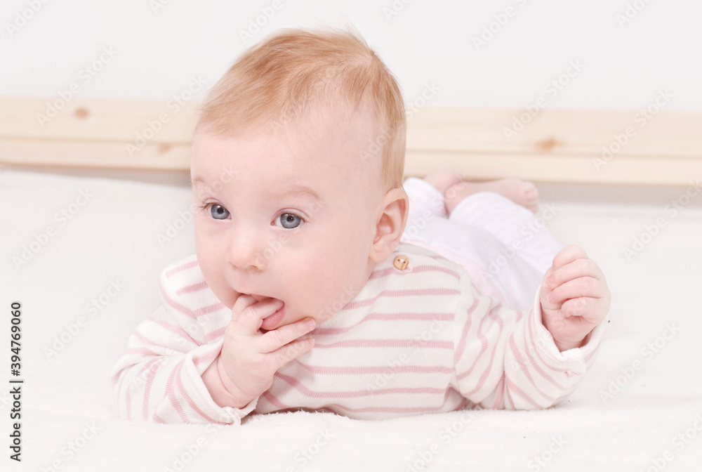 Cutest little 4 month old caucasian baby girl in striped T-shirt putting fingers in mouth. Baby health concept. Cutest little 4 month old caucasian baby girl in striped T-shirt putting fingers in mouth. Baby health concept.