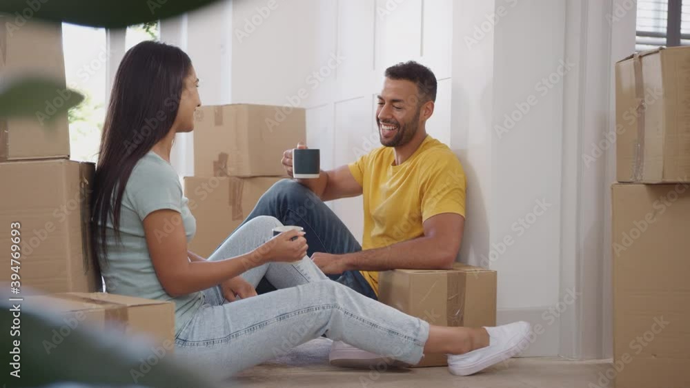 Couple taking a break on moving day sitting on floor surrounded by boxes and making a toast with hot drinks - shot in slow motion Couple taking a break on moving day sitting on floor surrounded by boxes and making a toast with hot drinks - shot in slow motion