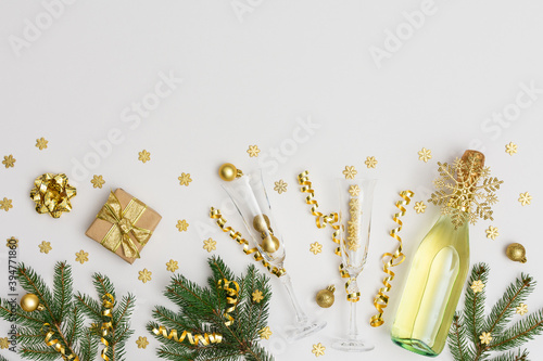 Festive background with gold decoration , bottle of sparkling wine with two crystal glasses, green spruce branches and shiny golden serpentine confetti ,glittering snowflakes and gift box, copy space