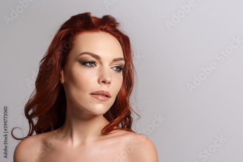 Beauty portrait of a red-haired beautiful woman on a gray background. Place for copyspace.