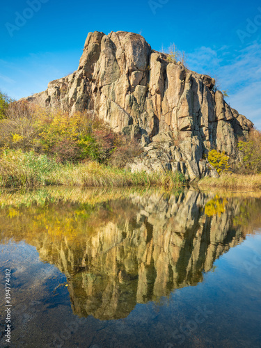 giant rock in sun lights with reflection in river under blue sky